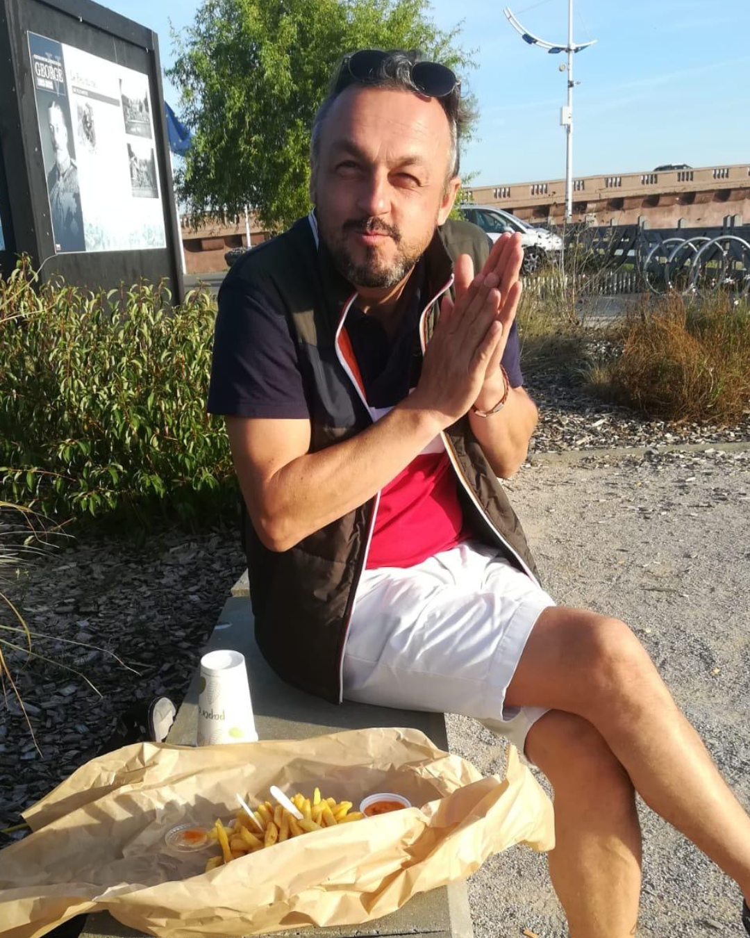 Nicolas Van Caemerbeke, assis au soleil sur un banc du port d'Étaples-sur-Mer, les mains jointes, devant une barquette de frites.