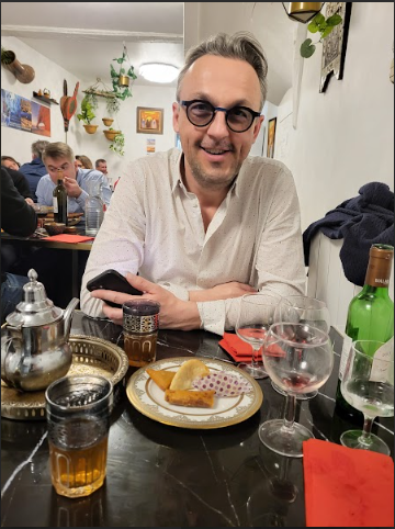 Nicolas Van Caemerbeke, souriant, attablé au restaurant devant un thé à la menthe et une assiette de pâtisseries.