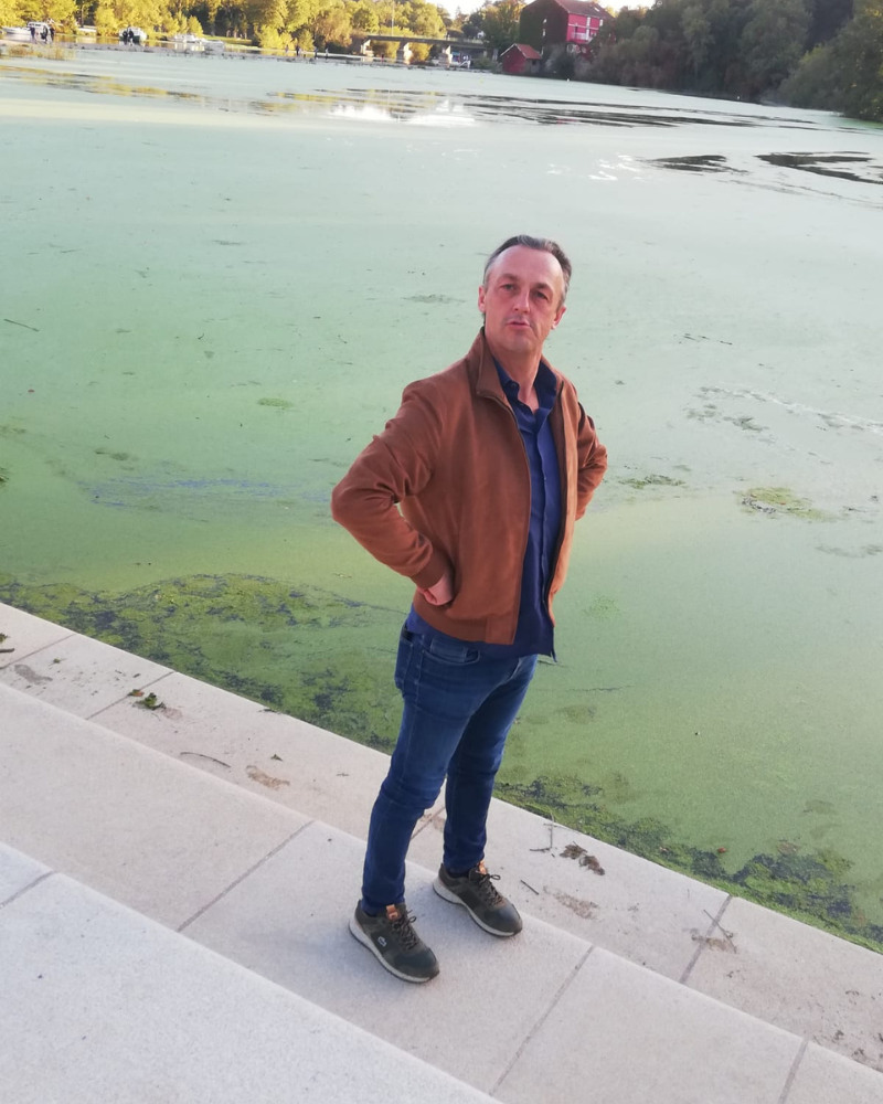 Nicolas Van Caemerbeke, les mains sur les hanches, debout sur un quai au bord d'un plan d'eau.