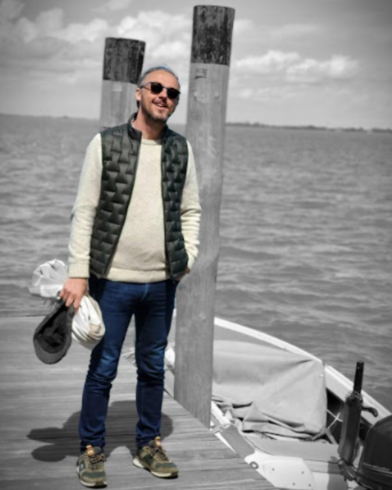 Nicolas Van Caemerbeke, souriant, debout sur un ponton au bord de l'eau, une casquette à la main.